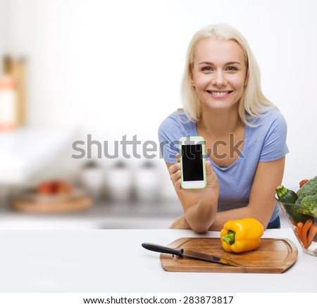 healthy eating, vegetarian food, dieting and people concept - smiling young woman cooking vegetables and showing blank smartphone screen over kitchen background