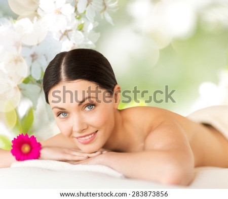 people, beauty, spa and body care concept - happy beautiful woman lying on massage desk over green natural cherry blossom background