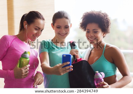 fitness, sport, training, gym and lifestyle concept - group of happy women with bottles and smartphone in gym