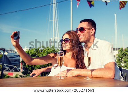 love, dating, people and holidays concept - smiling couple wearing sunglasses drinking champagne and making selfie at cafe