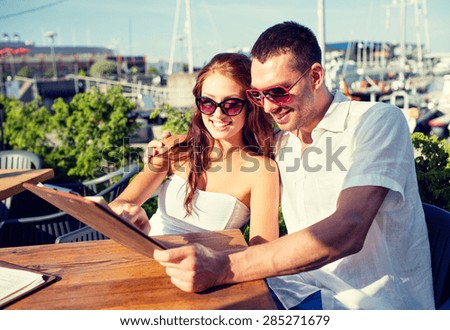 love, dating, people and food concept - smiling couple wearing sunglasses looking at menu on cafe terrace