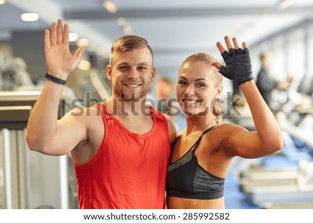 sport, fitness, lifestyle, gesture and people concept - smiling man and woman waving hands in gym