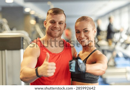 sport, fitness, lifestyle, gesture and people concept - smiling man and woman showing thumbs up in gym
