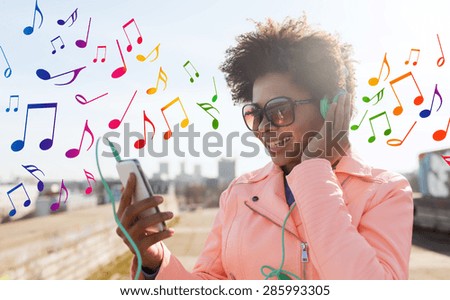technology, lifestyle and people concept - smiling african american young woman or teenage girl with smartphone and headphones listening to music outdoors over colorful musical notes background