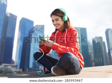 technology,  travel, tourism and people concept - smiling young woman or teenage girl with smartphone and headphones listening to music over singapore city background
