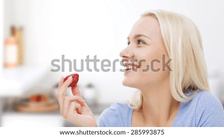 healthy eating, food, fruits, diet and people concept - happy woman eating strawberry over kitchen background