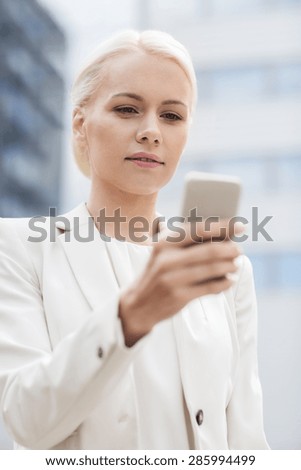 business, technology and people concept - serious businesswoman with smartphone over office building