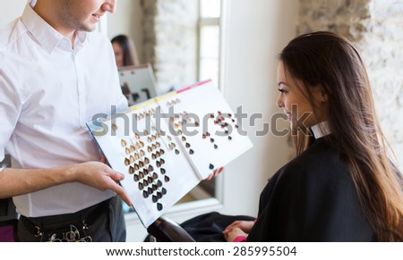 beauty, hair dyeing and people concept - happy young woman with hairdresser choosing hair color from palette samples at salon