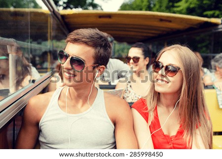 friendship, travel, vacation, summer and people concept - smiling couple with earphones traveling by tour bus
