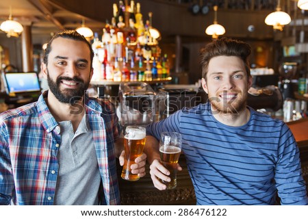 people, leisure, friendship and bachelor party concept - happy male friends drinking beer and talking at bar or pub