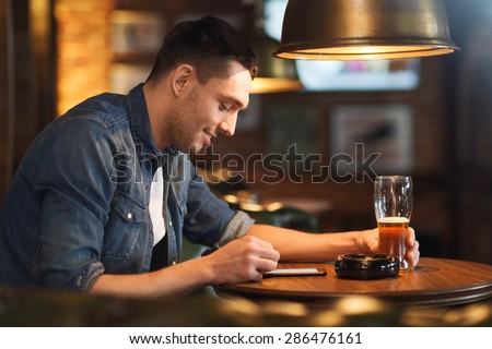 people and technology concept - happy man with smartphone drinking beer and reading message at bar or pub