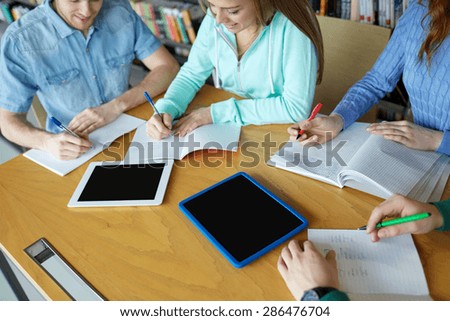 people, knowledge, education and school concept - group of happy students with tablet pc computers writing to notebooks in library