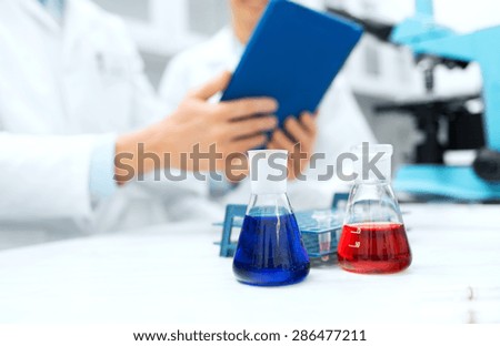 science, chemistry, technology, biology and people concept - close up of scientists with glass tes flasks and tablet pc computer on table in lab