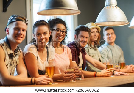 people, leisure, friendship and communication concept - group of happy smiling friends drinking beer, water or cocktails at bar or pub