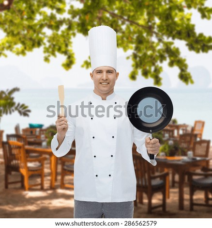 cooking, profession and people concept - happy male chef cook holding frying pan and spatula over restaurant lounge on beach
