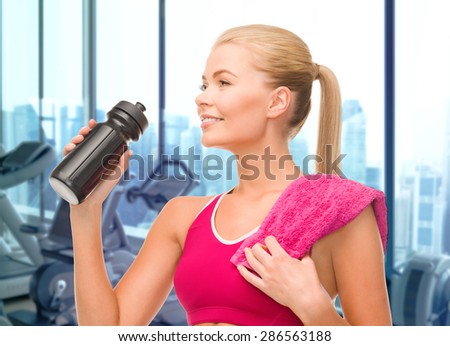 people, sport, fitness and recreation concept - happy woman drinking water from bottle with towel over gym machines background
