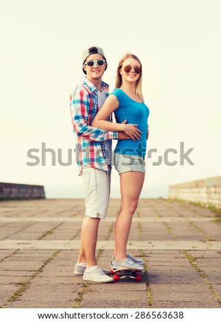 holidays, vacation, love and friendship concept - smiling couple with skateboard outdoors