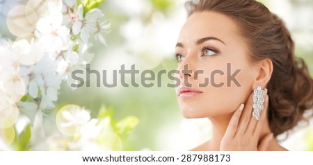 people, beauty, jewelry and accessories concept - beautiful woman with diamond earrings over summer garden and cherry blossom background