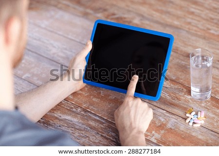 medicine, technology, nutritional supplements and people concept - close up of male hands pointing finger to blank tablet pc computer screen , pills and water on table