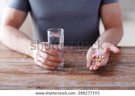 healthy lifestyle, medicine, nutritional supplements and people concept - close up of male hands holding pills with cod liver oil capsules and water glass