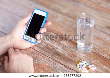 medicine, technology, nutritional supplements and people concept - close up of male hands smartphone, pills and water on table