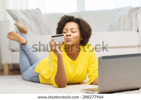 people, internet bank, online shopping, technology and e-money concept - happy african american young woman lying on floor with laptop computer and credit card at home