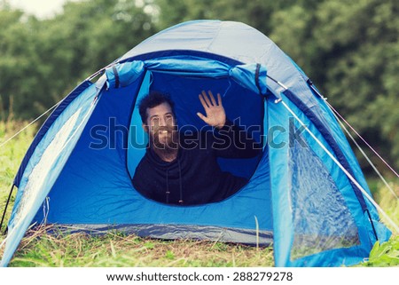 camping, travel, tourism, hike and people concept - smiling male tourist with beard waving hand in tent