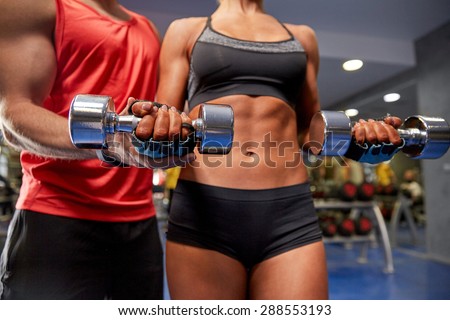 fitness, sport, exercising and weightlifting concept - young woman and personal trainer with dumbbells flexing muscles in gym