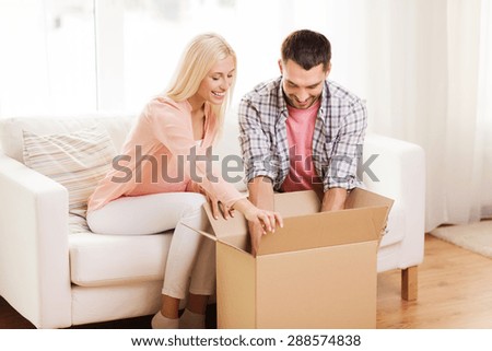 people, delivery, shipping and postal service concept - happy couple opening cardboard box or parcel at home