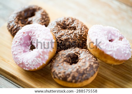 food, junk-food and eating concept - close up of glazed donuts on wooden board
