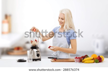 healthy eating, cooking, vegetarian food, dieting and people concept - smiling young woman putting fruits and berries for fruit shake to blender shaker over kitchen background