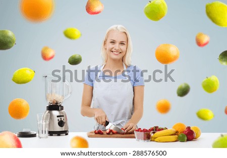 healthy eating, cooking, vegetarian food, dieting and people concept - smiling young woman with blender chopping fruits and berries for fruit shake over gray background with falling vegetables