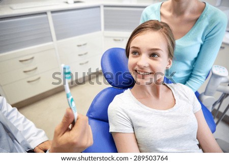 people, medicine, stomatology and health care concept - happy male dentist showing toothbrush to patient girl and her mother at dental clinic office