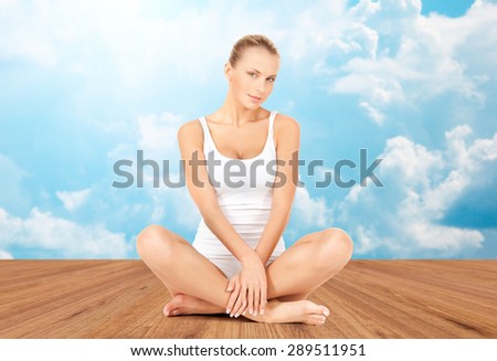 wellness, health and people concept - beautiful young woman in cotton underwear sitting on wooden floor over white clouds and blue sky background