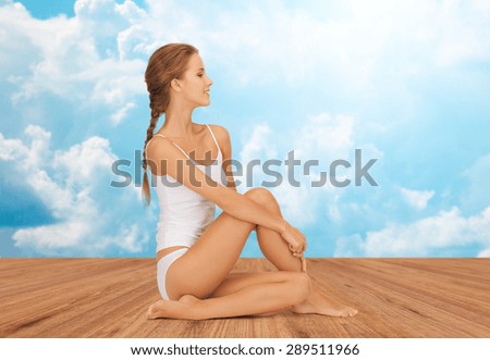 wellness, health and people concept - beautiful young woman in cotton underwear sitting on wooden floor over white clouds and blue sky background