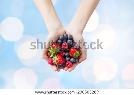 healthy eating, dieting, vegetarian food and people concept - close up of woman hands holding different ripe summer berries over blue lights background