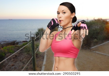 people, sport, fitness, jogging and healthy lifestyle concept - happy asian woman coach blowing whistle outdoors over beach sunset background