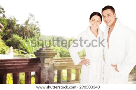 people, travel, tourism, vacation and honeymoon concept - happy couple in bathrobes over spa hotel resort background