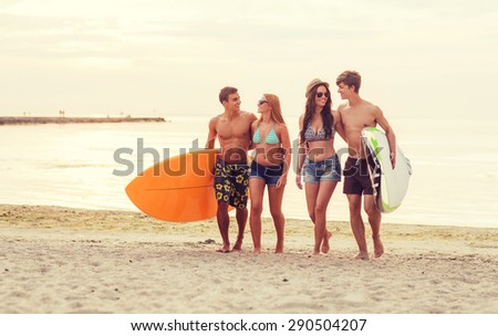 friendship, sea, summer vacation, water sport and people concept - group of smiling friends wearing swimwear and sunglasses with surfboards on beach