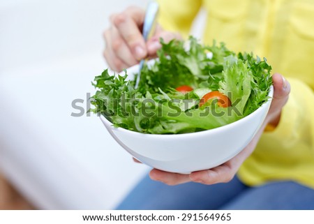 healthy eating, dieting and people concept - close up of young woman eating vegetable salad at home