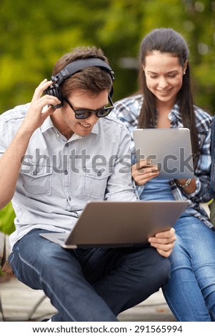 summer, communication, technology , education and teenage concept - group of students or teenagers in headphones with laptop and tablet pc computers at park or campus