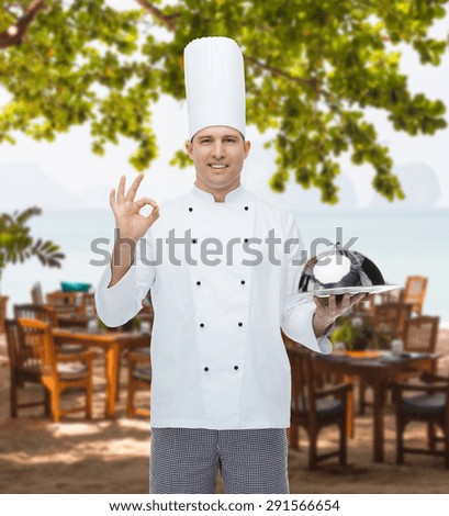 cooking, profession, gesture and people concept - happy male chef cook holding cloche and showing ok sign over restaurant lounge on beach
