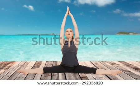 people, health, wellness and sport concept - happy young woman in yoga pose on wooden floor over sea and blue sky background