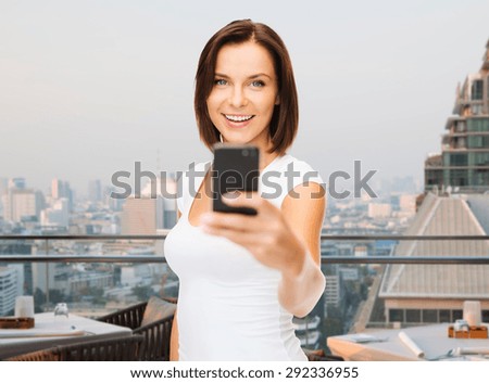 people, technology, tourism and travel concept - young woman taking selfie with smartphone over singapore city background