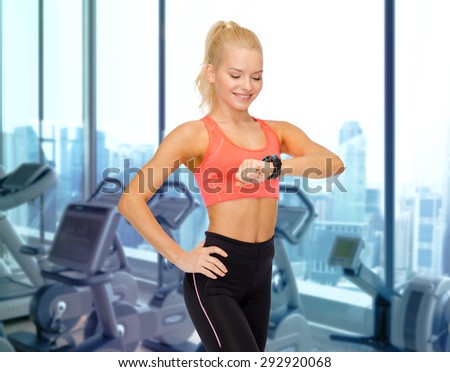 fitness, sport, technology, people and exercising concept - smiling woman looking at heart rate watch on hand over gym machines background