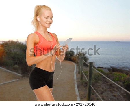 sport, fitness, technology and people concept - smiling sporty woman with smartphone and earphones listening to music over beach sunset background