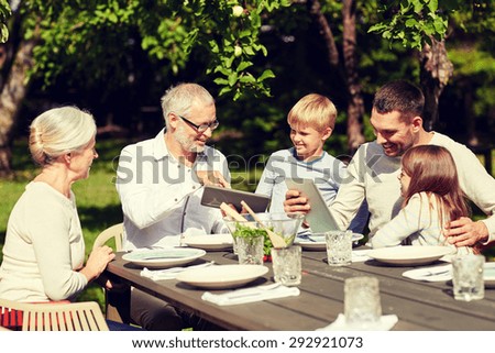 family, generation, technology, home and people concept - happy family with tablet pc computers sitting at table in summer garden