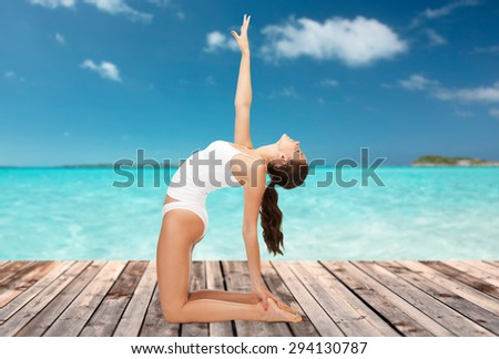 people, health and wellness concept - woman in cotton underwear doing yoga exercise on wooden floor over sea and blue sky background