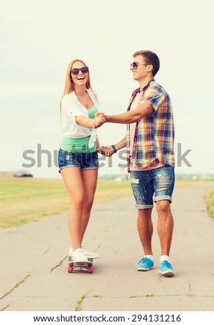 holidays, vacation, love and friendship concept - smiling couple with skateboard riding and holding hands outdoors