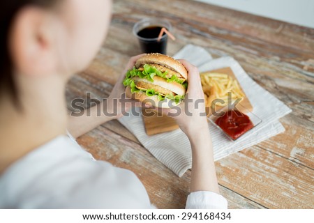 fast food, people and unhealthy eating concept - close up of woman hands holding hamburger or cheeseburger
